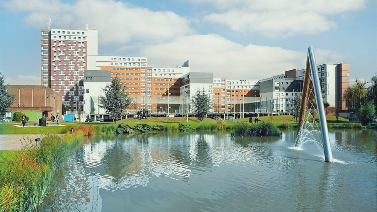 An image of Aston University buildings next to a lake with a fountain. 