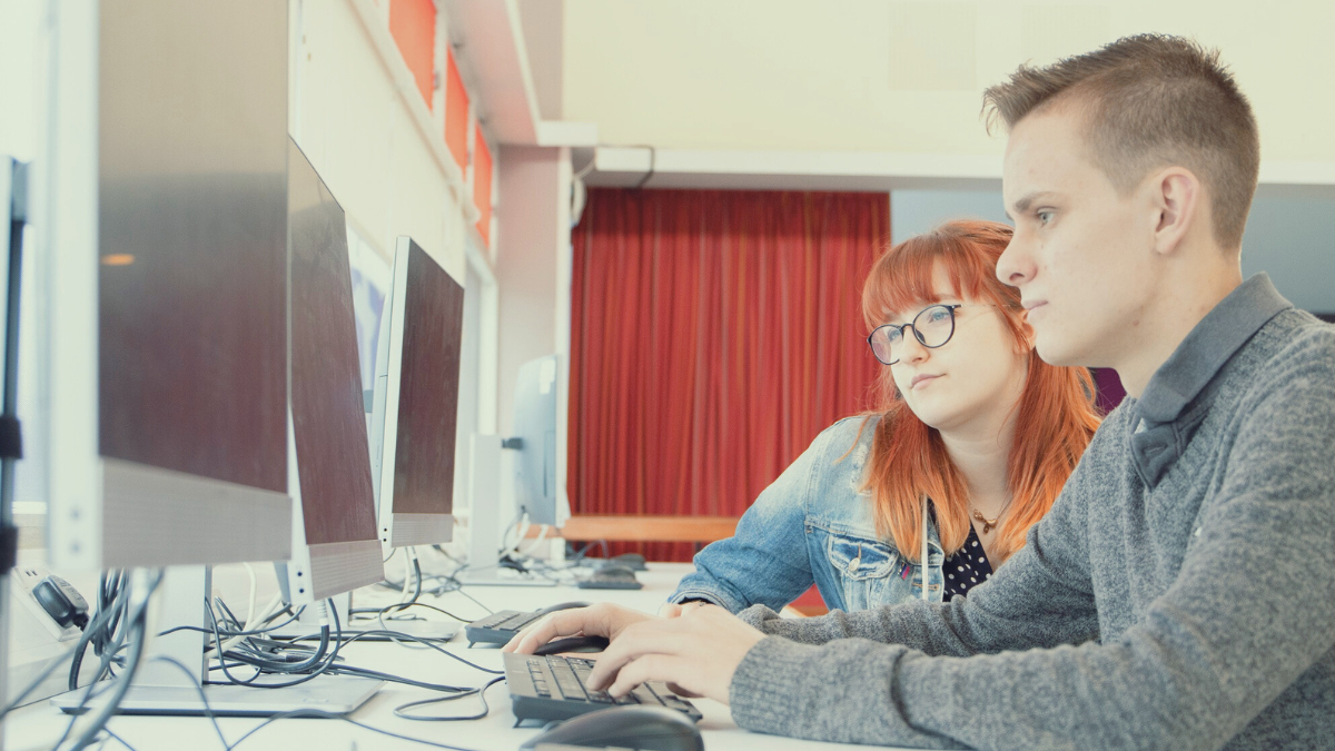 Two students at a desk looking at a computer screen together.