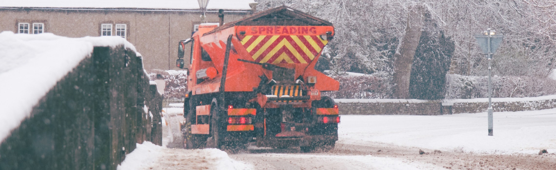 Gritting truck spreading salt on road covered in heavy snow